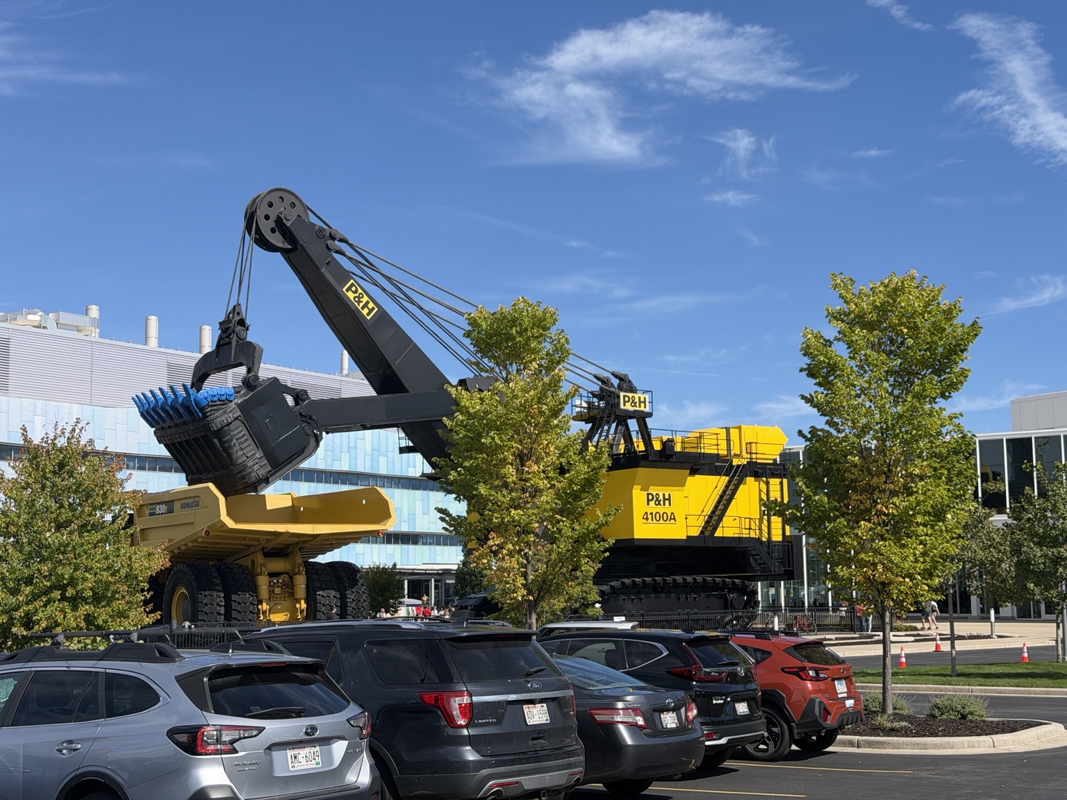 A large yellow P&H mining shovel and Komatsu haul truck displayed outside Komatsu’s Milwaukee facilities beneath a blue sky.