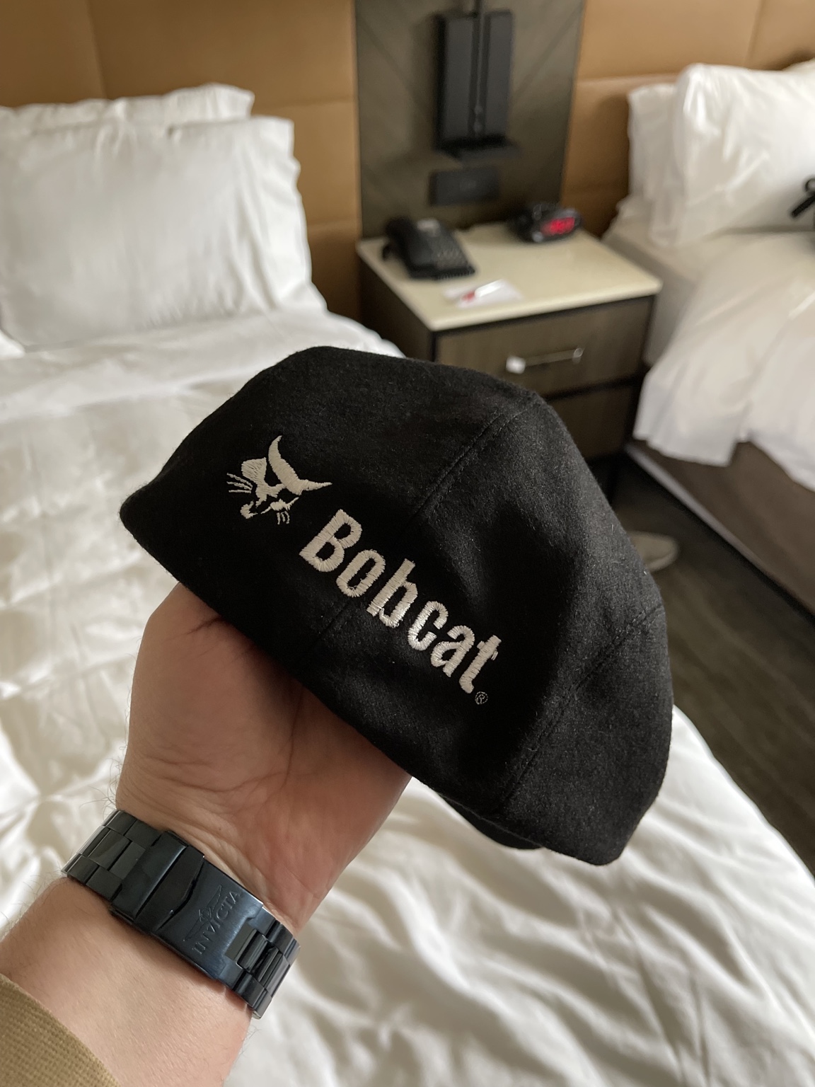 Aaron holding his custom black flat cap with white Bobcat embroidery, a gift from his friends on the Bobcat product safety team.